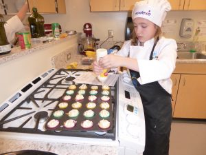 Child squeezing frosting onto cupcakes