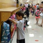 Elementary student hanging up backpack in school hallway